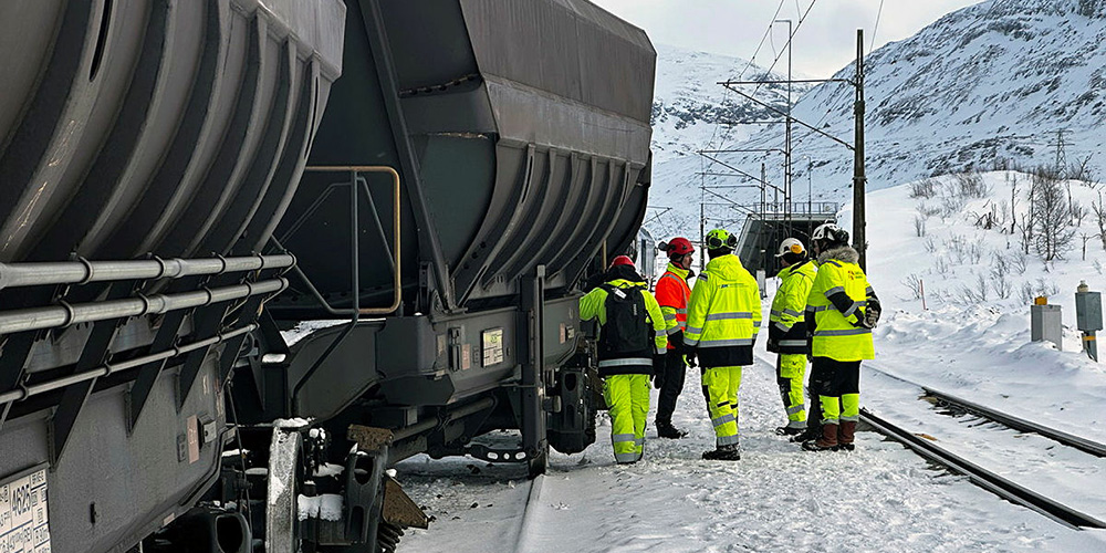 Four persons in high visibility clothing alongside a goods train.