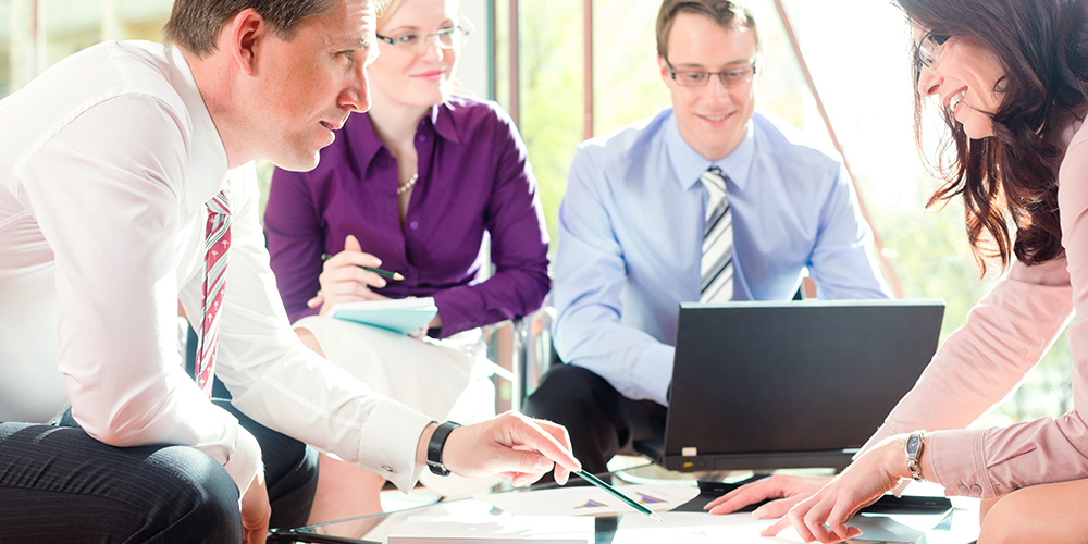 Four persons interacting at a table with a laptop.