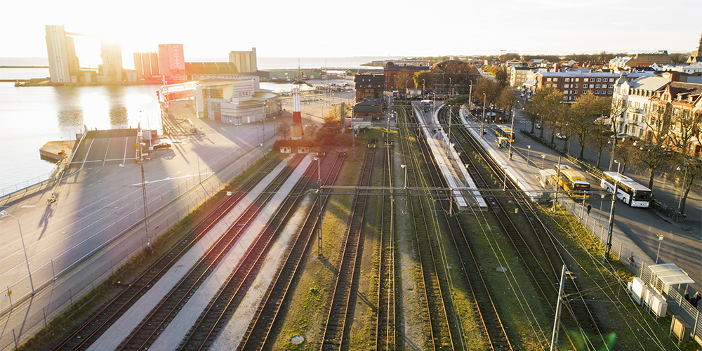 Drönarbild över järnväg och väg i stad i sol.