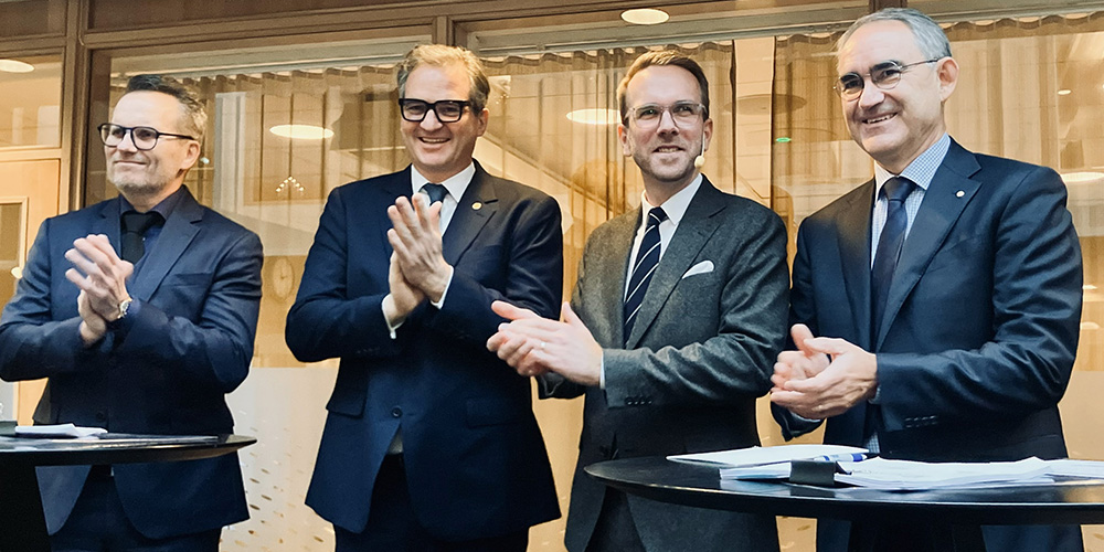 Fyra män i kostym står och  klappar händerna.