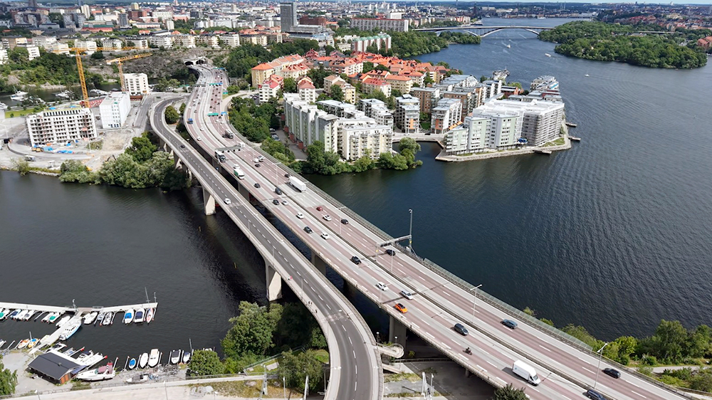 Flygbild över Essingeleden. En flerfilig väg som går över vatten. Bebyggelse i bakgrunden.